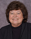 Marita Inglehart - older White woman with black sweater smiling, short dark curly hair