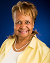 Wendy Woods - older African American woman with short blonde hair, smiling, wearing yellow collared shirt, white necklace, and white shirt underneath.