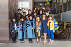 Group of CEW+ scholars in graduation robes posed together on the front stairs of CEW+